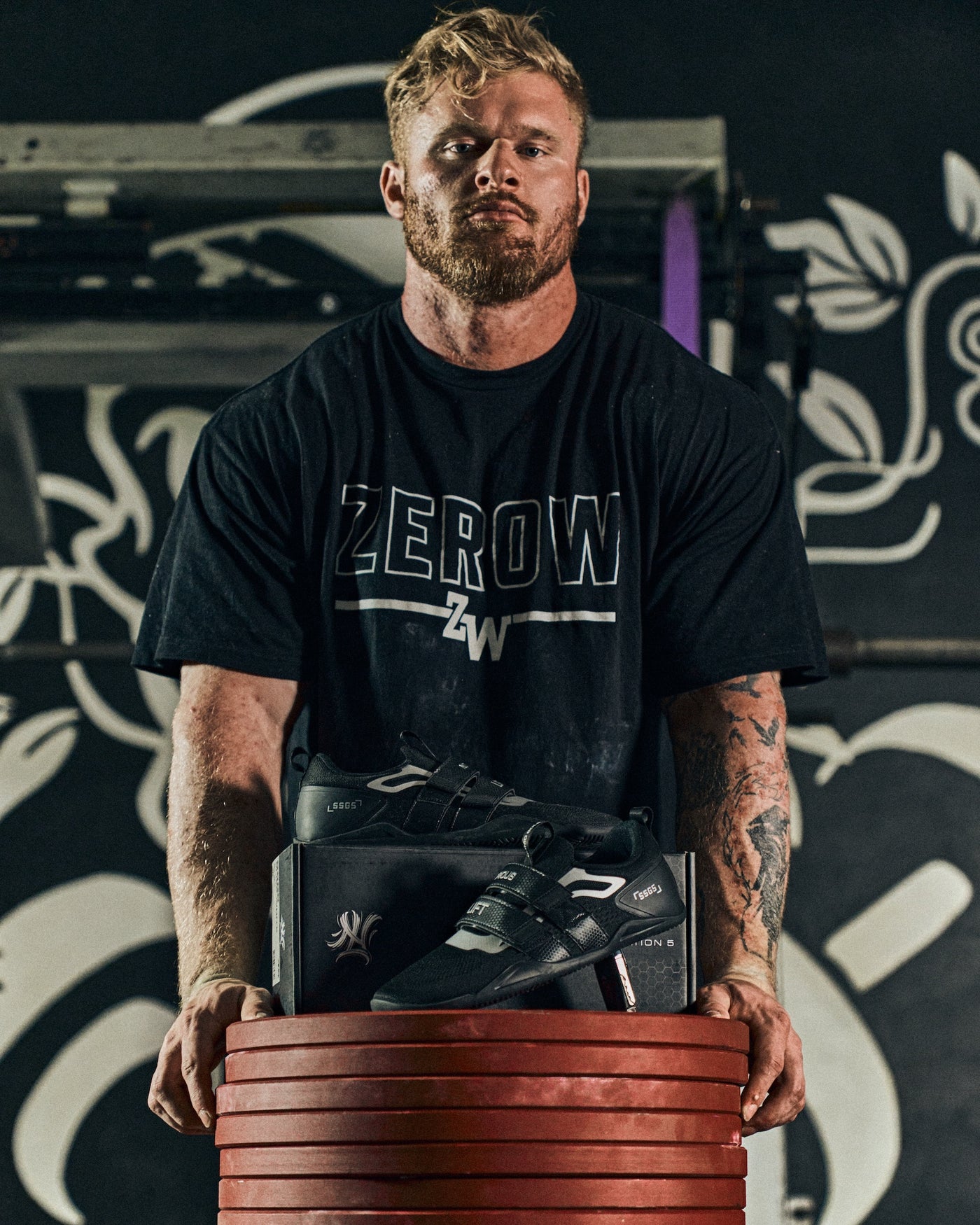 Notorious Lift athlete with Sumo Sole Gen 5 lifting shoes on red weight plates in gym setting